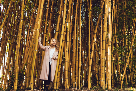 beautiful girl in a pink coat stands near a tall bamboo tree, posing and enjoying the springの写真素材