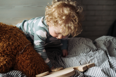 little curly-haired boy sitting in bed and playing with his toysの写真素材