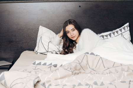 cute young girl in pajamas lying in bed, resting after a hard day's work, smilingの写真素材