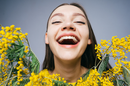 cheerful young girl holding a fragrant yellow mimosa, laughing and enjoying the springの写真素材