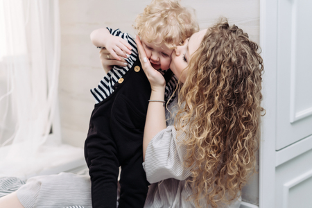 curly-haired young mother kisses her little son child, loves himの写真素材