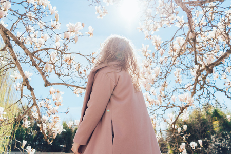 curly young woman in a trendy pink coat walking in a park in the sun, enjoying the warmthの写真素材