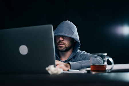 mysterious bearded man hides his face under the hood and hacks the password on the laptop in the darkの写真素材