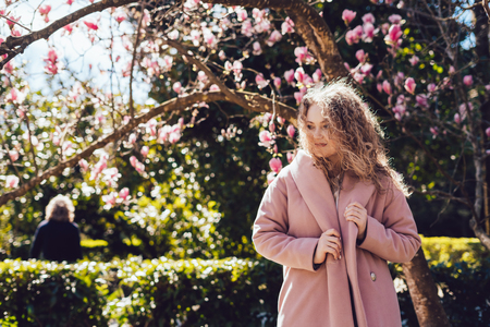 stylish young woman in pink coat enjoying spring heat and sun in park, posingの写真素材