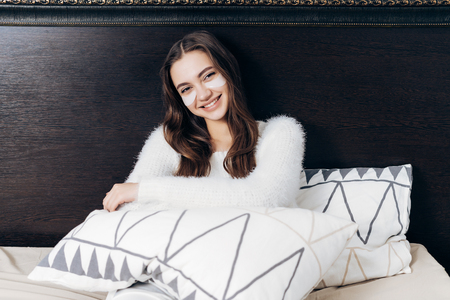 beautiful happy girl in pajama sits in bed early in the morning, under eyes with white patches, smilingの写真素材
