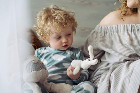 small curly baby boy in blue pajamas sitting next to mom playing with toysの写真素材