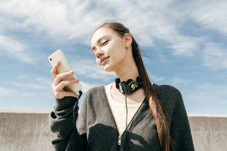 attractive stylish girl in black sportswear looks into her smartphone, resting outdoorsの写真素材