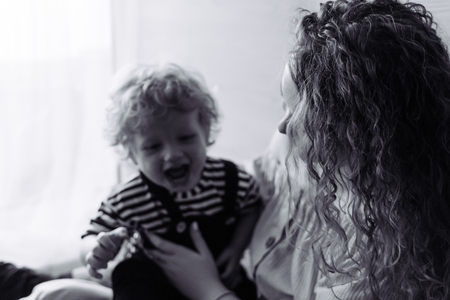 curly young mother playing with her little son, laughing and having funの写真素材