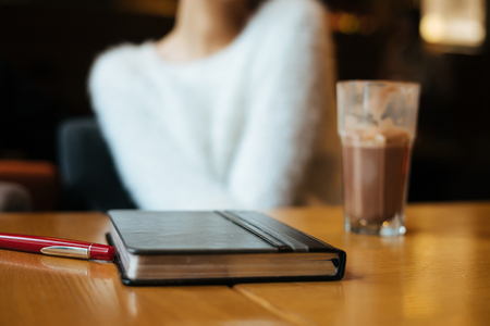 girl in a white sweater sits in a cafe at the table, lies a notebook with important notesの写真素材
