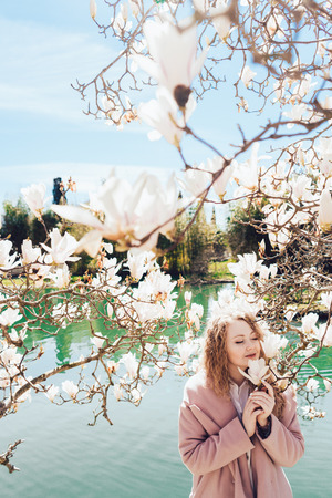 beautiful young woman enjoys the warmth and sun in the park next to the pond and magnoliaの写真素材