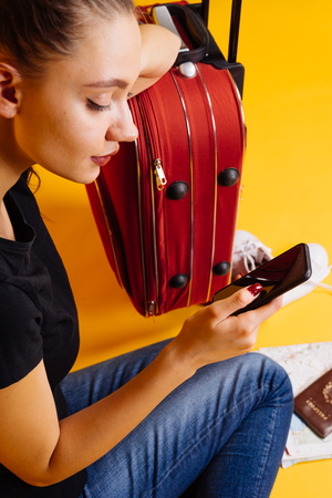 beautiful young woman goes on a round-the-world trip with a large suitcase, looks into her smartphoneの写真素材