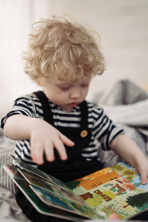 little curly baby boy looking at book, studying the worldの写真素材