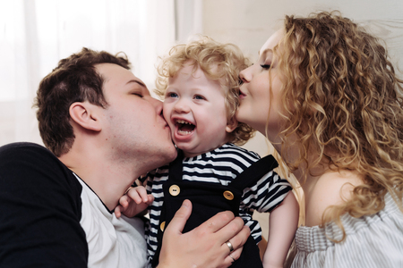 friendly cheerful family, young parents, father and mother hug their little curly-haired son