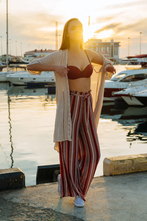 a young girl in stylish summer clothes is waiting for her yacht in the port in the rays of the evening sun, a long-awaited vacationの写真素材