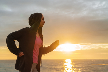 confident young girl in a sweatshirt runs along the sea embankment in the evening, prepares for a marathonの写真素材