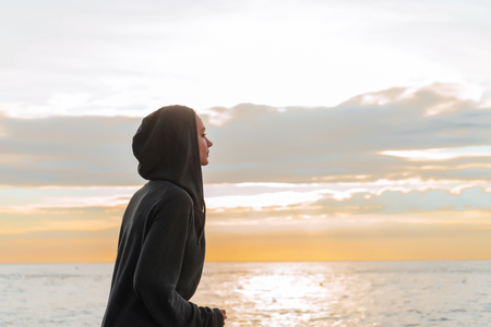 a young girl in a hood is engaged in jogging at sunset on the sea promenade, wants to lose weightの写真素材