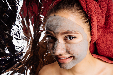 beautiful young girl with a red towel on her head applied a useful cleansing mask on her face, smilingの写真素材