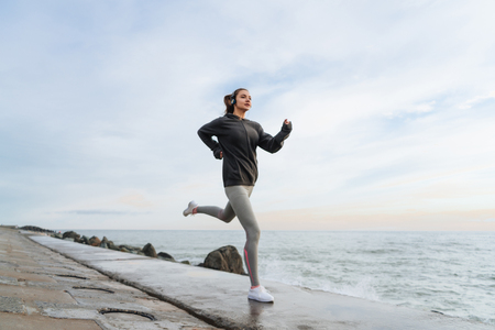 fast sports girl jogging by the sea, listening to music on headphonesの写真素材