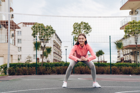 active smiling girl in a pink sweater trains and squats on a sports fieldの写真素材