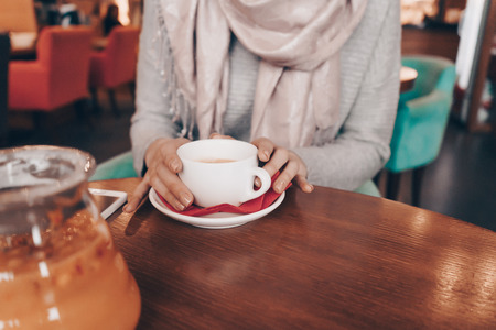 a girl with a headscarf on her head sits in a cozy restaurant, drinks fragrant tea and waits for someoneの写真素材