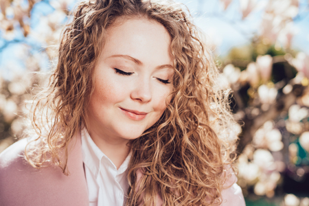 lovely curly-haired woman smiling, closing her eyes, enjoying the warm spring weather and the sunの写真素材