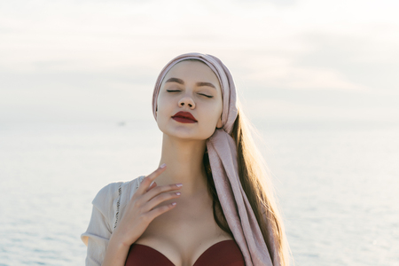 a luxurious, peaceful girl with a headscarf on her head enjoys the warmth and sea voyage, closed her eyesの写真素材