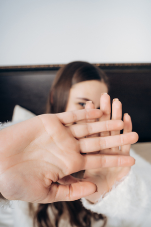 embarrassed young girl sitting on the bed, covering her face with her hands and laughingの写真素材