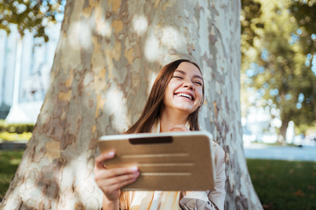 Girl worker resting in the park after work, laughing on something in tablet pc, use web cameraの写真素材