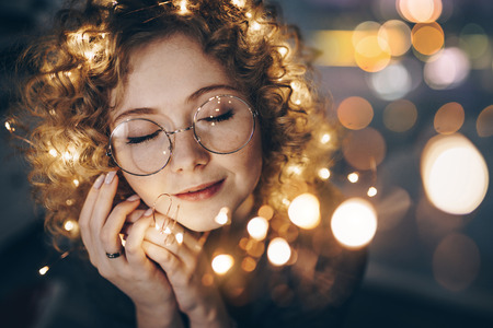 magic curly girl in blurry Christmas garlands dreaming, dreaming, waiting for a miracleの写真素材