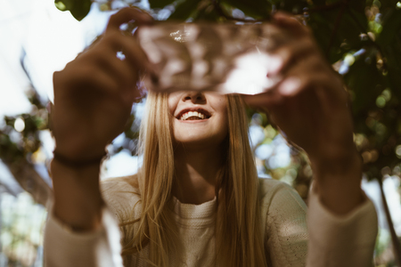 Smile of the girl looking at the phone. Playing the phone, the phone is blurred in the foregroundの写真素材