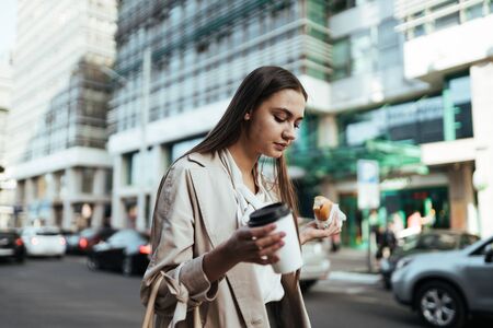 Business woman on the background of the metropolis holds in her hand a coffee and a sandwichの写真素材