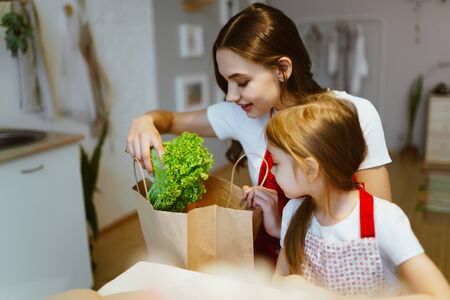 Mom and daughter take purchased vegetables in the kitchen from the packageの写真素材