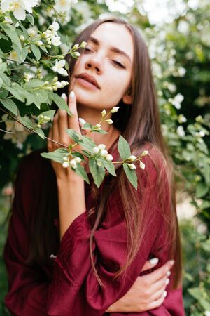 a beautiful gypsy with an expression of languor and pleasure touches her cheek on a flowering tree branchの写真素材