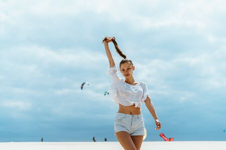 girl energetically walks along the beach stretching up her hand that holds her hairの写真素材