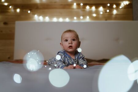 the baby is lying on the blanket and looking at the camera with surprised eyes, light bulbs sparkle aroundの写真素材
