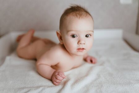 a baby without clothes lies on his tummy and looks up at the camera with his head raisedの写真素材