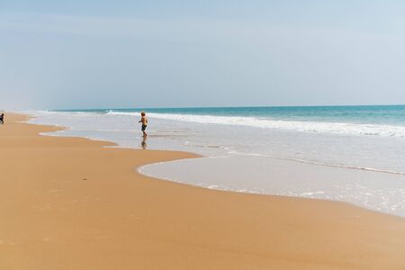a deserted beach, the ocean rolls its waters and one person stands at the water's edgeの写真素材