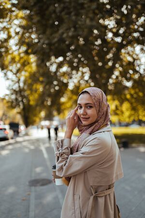 Muslim woman on a city street holds coffee and looks over her shoulderの写真素材