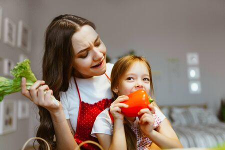 mom and daughter in the kitchen. daughter eats bell pepper, while mom looks with expression of despair. Allergy?の写真素材