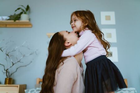 daughter hugged mom by the neck with her hands, and mom gently kisses her chinの写真素材