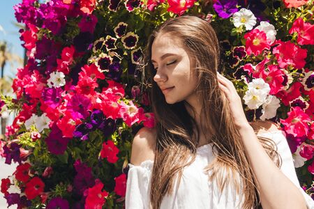 the summer girl among closed her eyes and leaned her head against the flowers of viola and petunia. very bright and sunnyの写真素材
