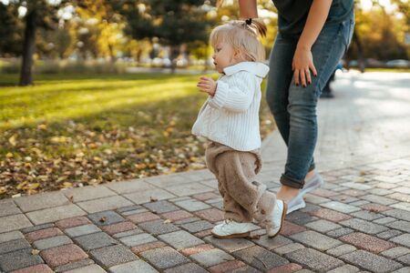 baby learns to walk, the first steps in the park by the handle with an adult