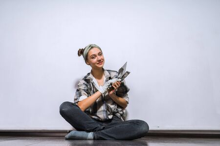 pretty woman in work clothes with repair tools sits in turkish against the background of the wallの写真素材