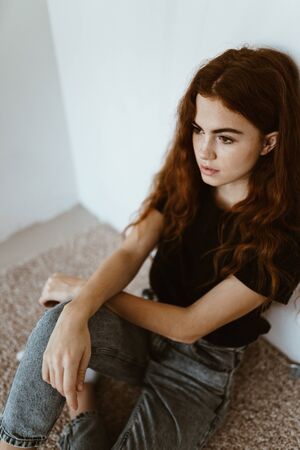 teenager girl in jeans and a T-shirt sits in a closed position not on the floor, leaning against the...