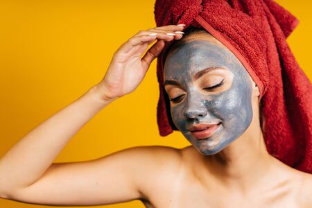 In self-isolation at home, the girl makes a cosmetic mask on her face, her hair covered with a towel mask black wall background yellowの写真素材