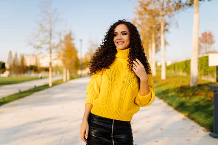 Portrait of a young smiling beautiful woman in a bright sweater against the blue sky and autumn trees. High quality photoの写真素材