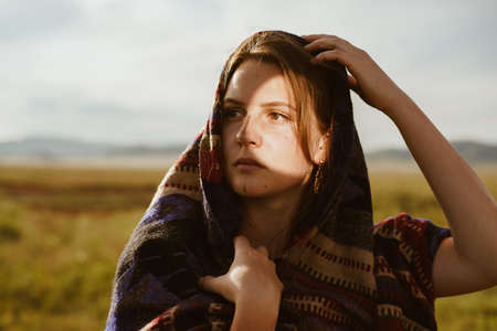 In the steppe, a girl of European appearance with a shawl over her head and shoulders with an...