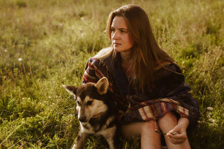 A young girl sits in a field with a dog. Dressed in a poncho, ethnic theme. High quality photo