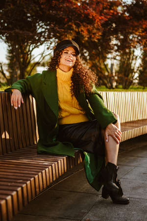 scarlet trees illuminated by the sun in the rays of which a gleefully smiling girl sits on a bench. High quality photoの写真素材