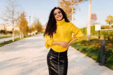 A woman in a leather skirt and a thick yellow sweater walks in the park stands cheering on the track. High quality photoの写真素材
